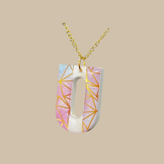 Aurielle är ett handgjort halsband i resin med rosa toner och gyllene geometriska detaljer. Ett unikt och elegant statement-smycke från kollektionen Divina.