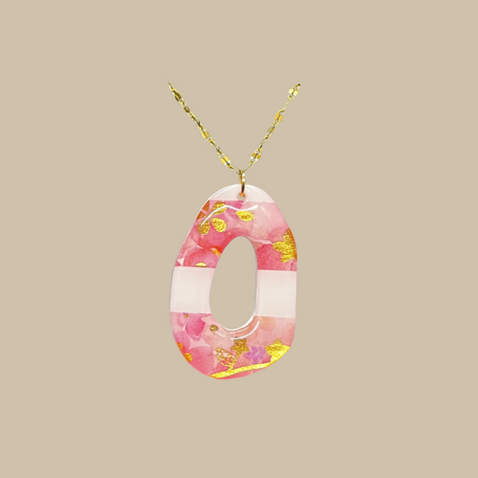 Elouise är ett handgjort halsband i harts med rosa toner och gyllene detaljer i ett elegant och konstnärligt uttryck. Ett unikt smycke från kollektionen Divina.