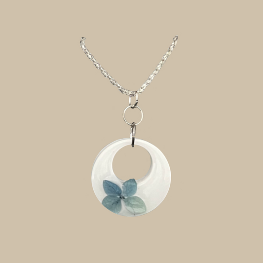 Elegant handgjort halsband med vit form och blå blomdetalj. Ett unikt smycke med mjukt och poetiskt uttryck.