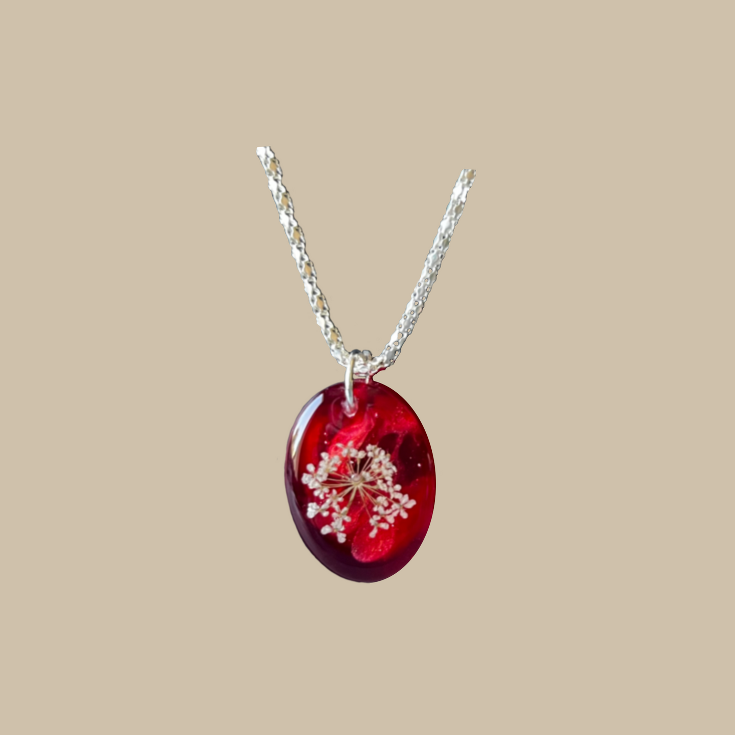 Handgjort halsband i djupa röda toner med vit blomdetalj. Ett romantiskt och unikt smycke med elegant oval form.