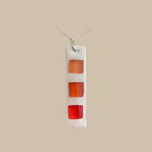 Valencia är ett handgjort halsband i resin med orange och röda grafiska detaljer. Ett modernt och unikt statement-smycke från kollektionen Divina.